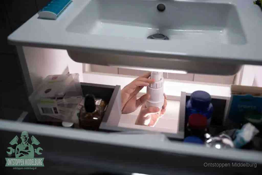 Een pompfles met zeep boven een wastafel, de heet water en afwasmiddel-methode om een vetprop in de afvoer los te maken in Middelburg