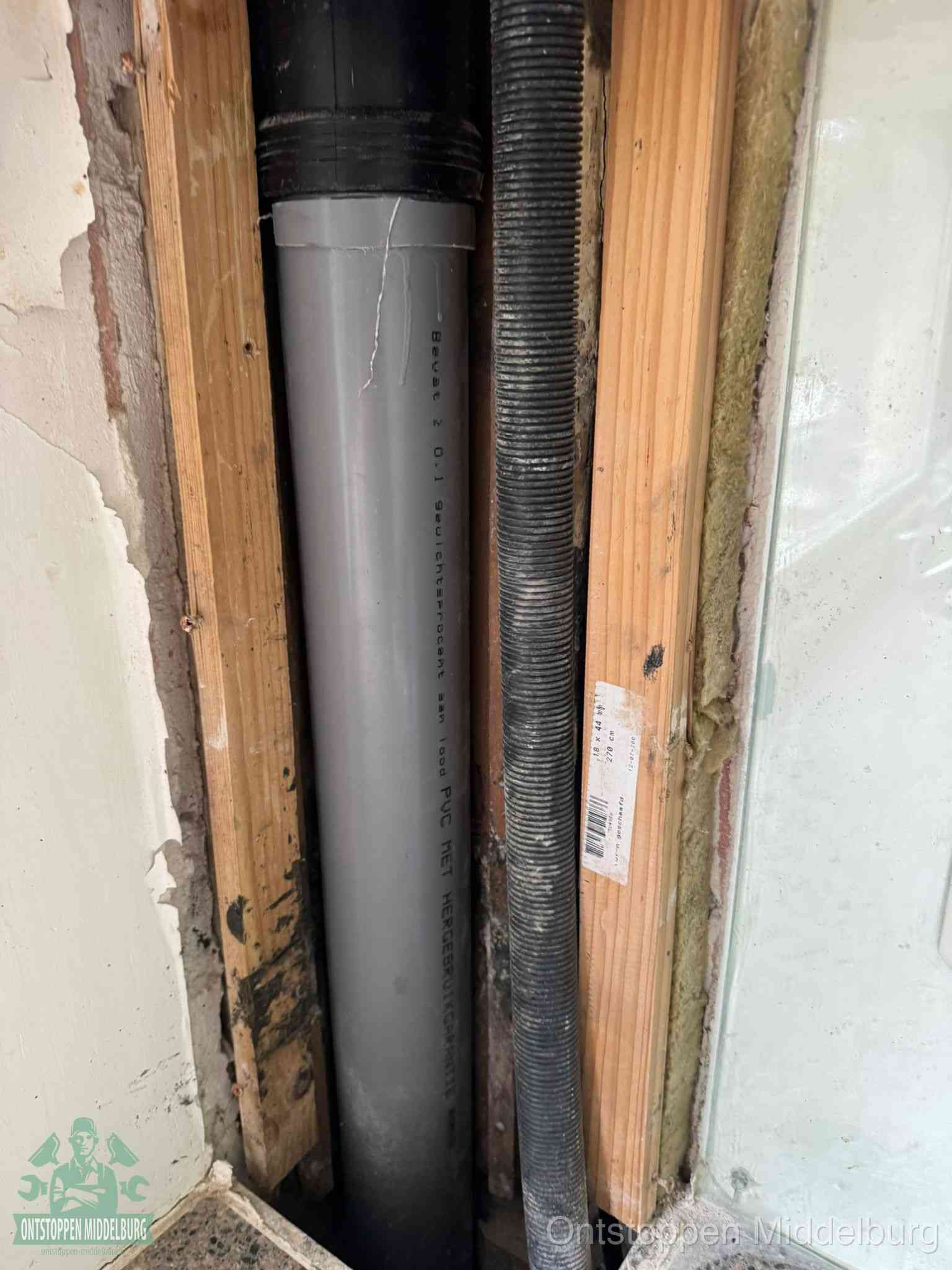 Een grijze PVC-afvoerbuis met een flexibele ribbelslang in een open wandconstructie, een verwaarloosde afvoer die te lang is blijven zitten in Middelburg