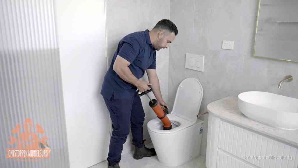 Een monteur buigt over een wandcloset en duwt met de hand een persluchtontstopper in de toiletpot om de verstopping handmatig los te maken in Middelburg
