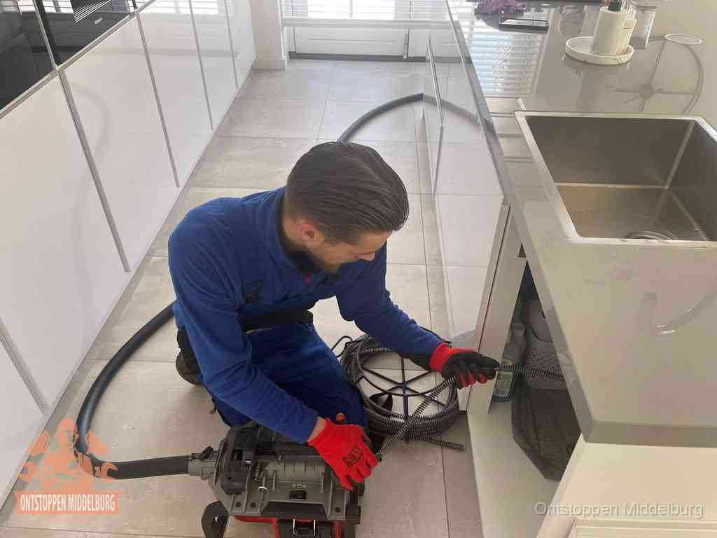 Een monteur ontstopt de keukenafvoer onder de spoelbak met een elektrische veermachine in Middelburg
