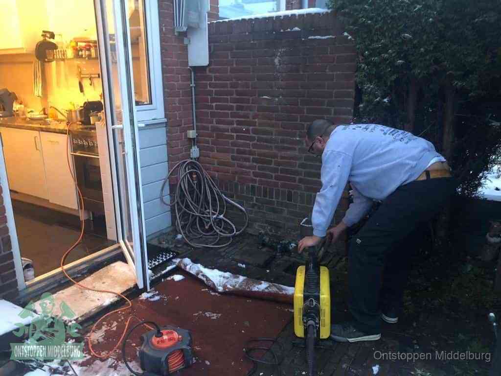 Een monteur werkt buiten bij een open riool-/grondput met een elektrische ontstoppingsmachine om een verborgen afvoerprobleem op te sporen in Middelburg
