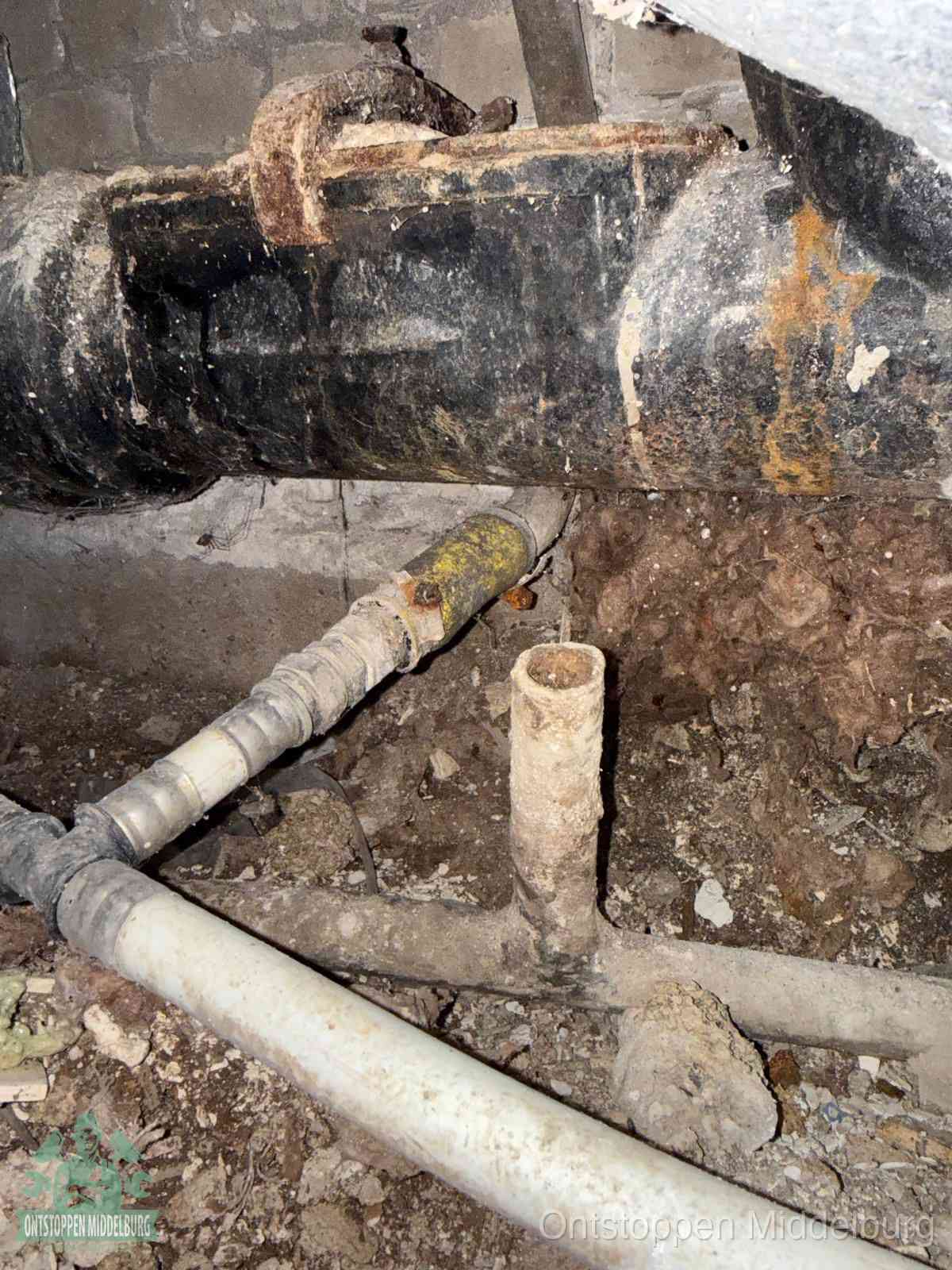 Een dikke zwarte hoofdrioolbuis met roest- en kalkaanslag in een kruipruimte, oorzaak van terugkerende structurele afvoerproblemen in Middelburg