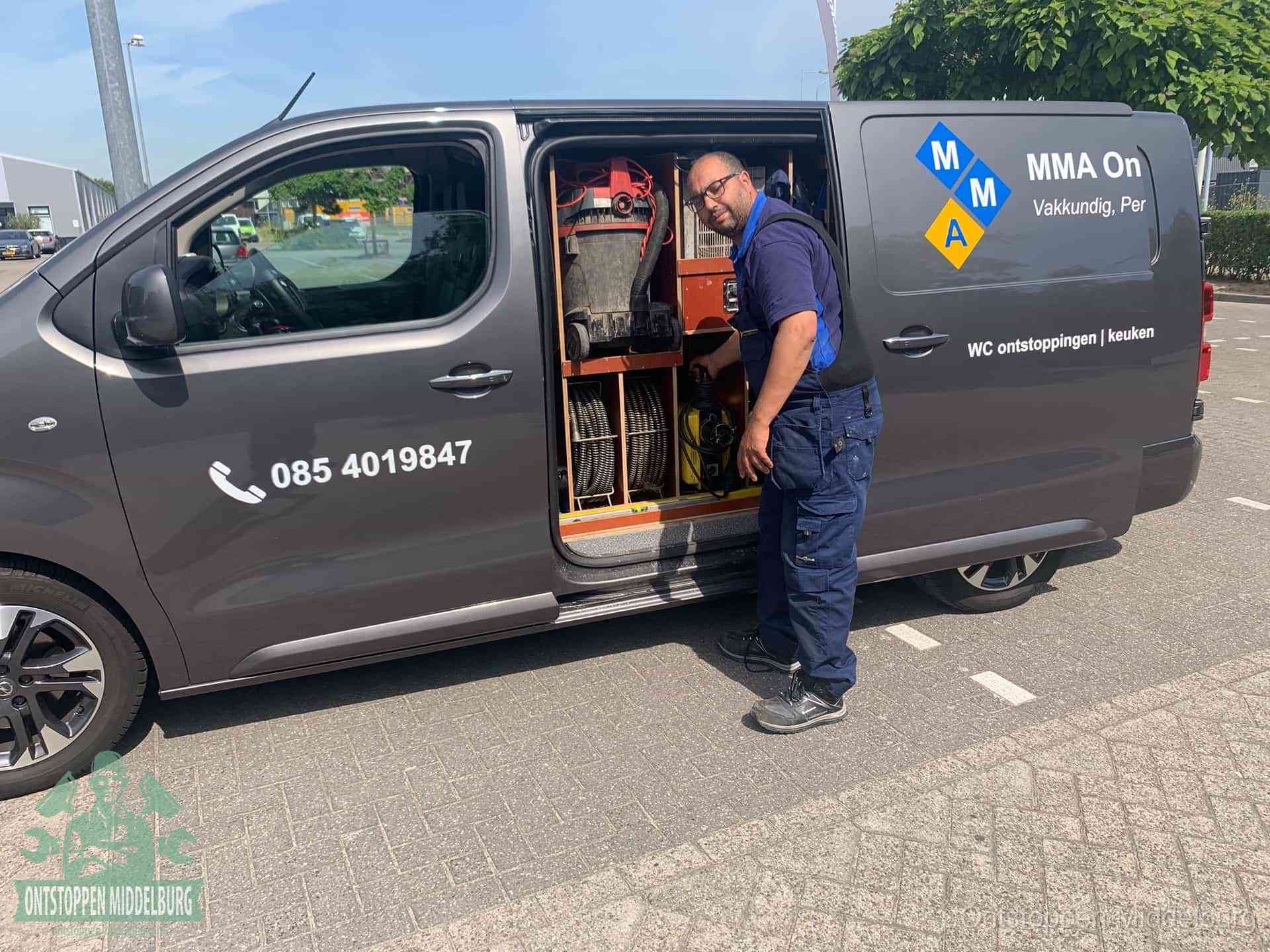 Een monteur bij de open schuifdeur van zijn bedrijfsbus op een parkeerplaats, klaar om de oorzaak van terugkerende afvoerverstoppingen aan te pakken in Middelburg
