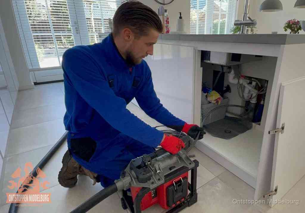 Een monteur voert een professionele elektrische ontstoppingsmachine in de afvoer onder de spoelbak tijdens het gootsteen ontstoppen in Middelburg